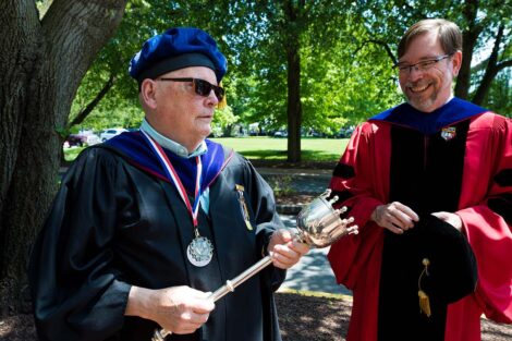 Prof. Ed Kerns and John Meier chat while wearing regalia with trees in background