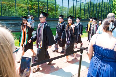 students in caps and gowns walk down brick pathway, Skillman behind them