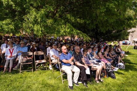 family members sit on folded chairs on the Quad under a tree for shade