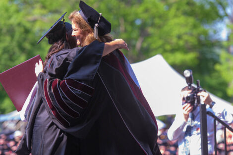 President Hurd hugs a student in cap and gown on stage