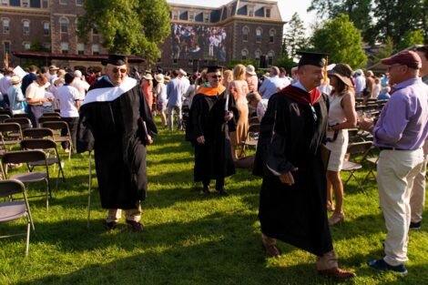 trustees in regalia walk on grass in the Quad away from the stage