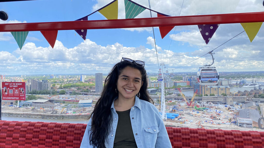 Denisse Villegas sits and smiles with a view of an international city behind her