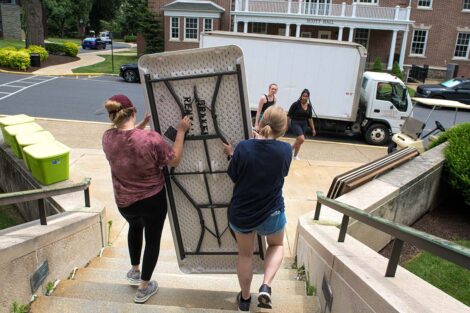 two students carry a folding table down stairs toward a moving truck
