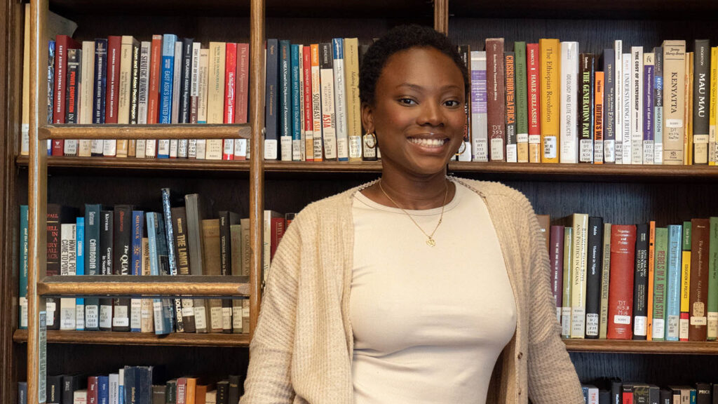 Mariatou Coulibaly '23 stands and smiles with bookshelves behind her
