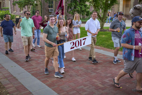 Alumni smile while walking in a parade, holding a 2017 banner