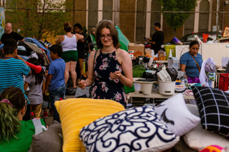 community members look through items, including colorful pillows, set out on tables