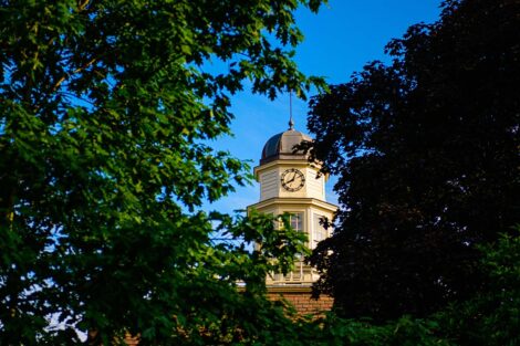 the cupola of Kirby House peaks through green leaves with a bright blue background
