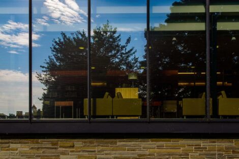 reflection of a bright blue sky and trees is seen through the glass windows of Skillman library