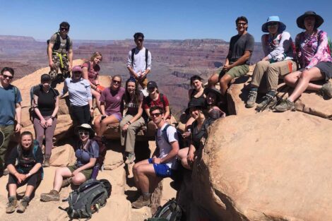 students sit on big rocks with backpacks and field notebooks
