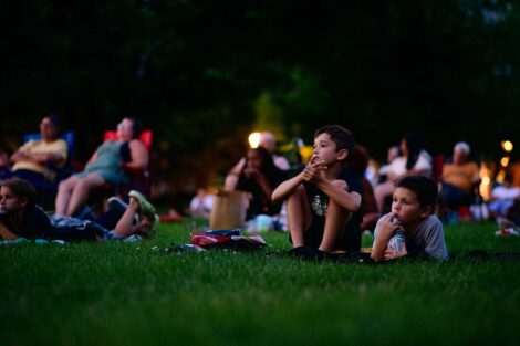 Children sitting on the lawn of the Quad and watching a free outdoor movie screening