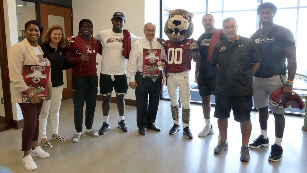 Lafayette College President Nicole Hurd, head football coach John Troxell, football team members, and Leopards mascot posing with Sal Panto, mayor of the city of Easton