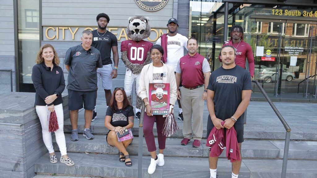 Lafayette College President Nicole Hurd, head football coach John Troxell, football team members, and Leopards mascot standing in front of the entrance to the Easton mayor's office building