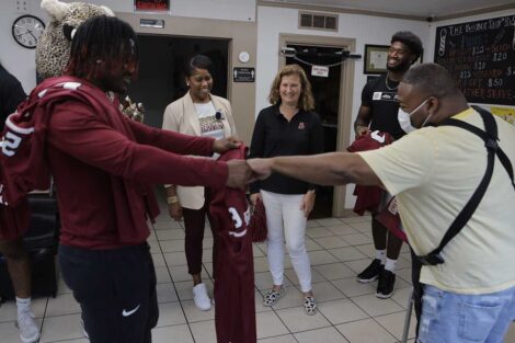 Lafayette College President Nicole Hurd, head football coach John Troxell, football team members, and Leopards mascot surprising owner of Barbershop Plus with free football tickets and jerseys
