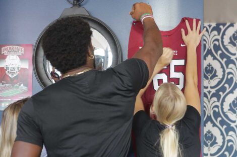 Lafayette football player helping Bayou restaurant employee hang up a Lafayette football jersey in the restaurant