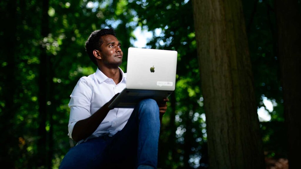 Lafayette student Areeb Atheeque sitting down outdoors and holding a laptop in front of a background of trees