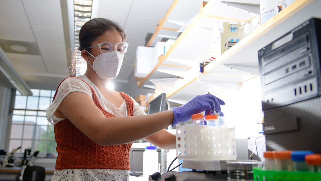 Anna DeFelice '24 works in a chemistry lab and holds a container of samples