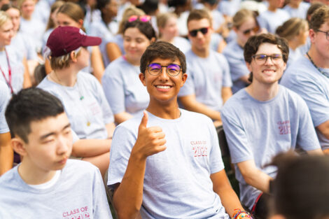 A student gives a thumbs up in a crowd.
