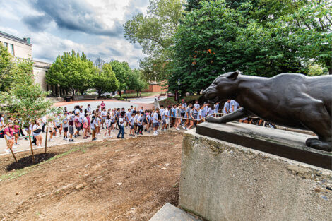 Students walk past a statue of a leopard.