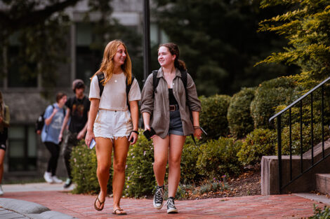 Students walk across the Quad, smiling.