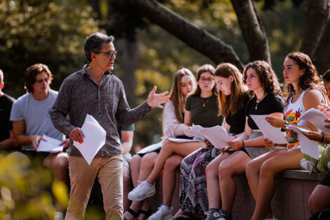 A professor holds class outside, speaking to their class surrounded by trees.