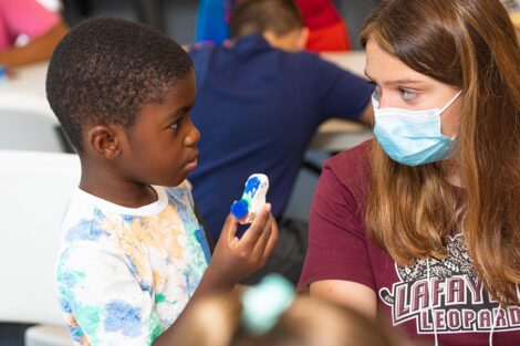 a Lafayette student in a mask makes eye contact with a young Easton student holding an arts and craft project