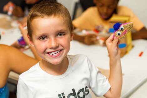 a young child smiles while holding an arts and crafts project