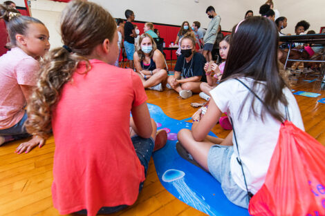 Lafayette students sit on the floor of a gymnasium with young children