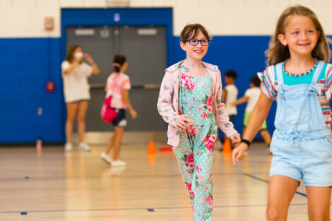 two young girls run in a gymnasium and smile