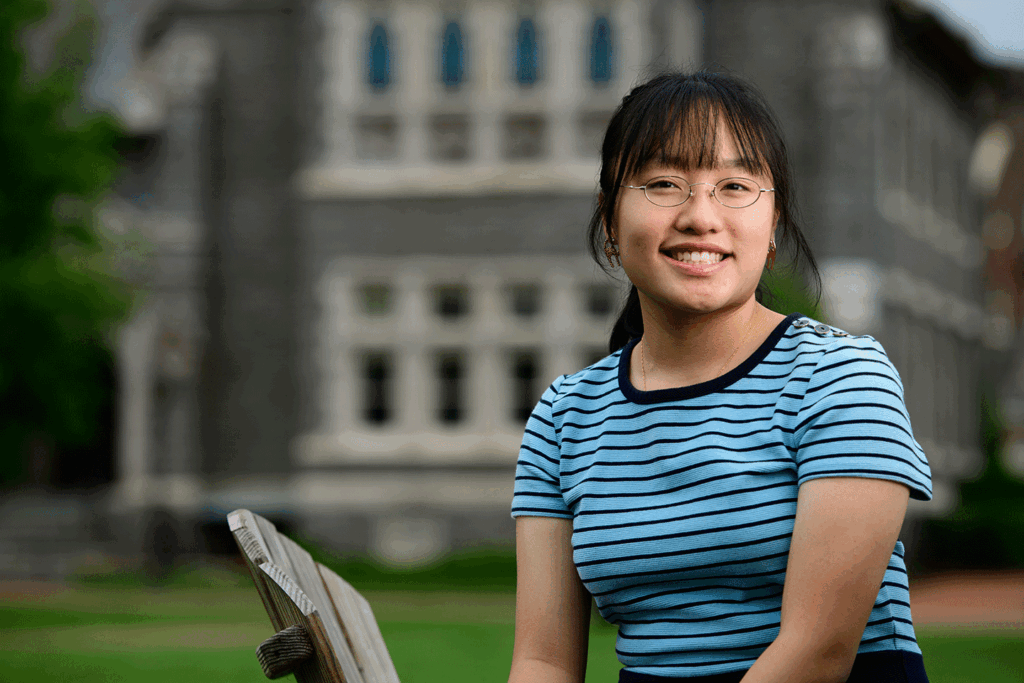 Camille Voo '26 is pictured outside on the Quad. She is sitting on a chair and wearing a blue t-shirt.