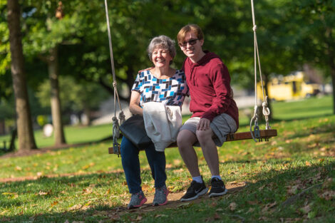 A student and their family member smile, sitting on a swing.