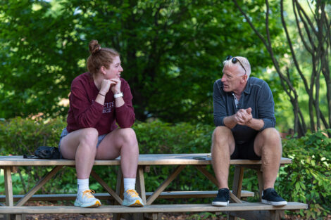 A student sits on a bench talking to a family member.