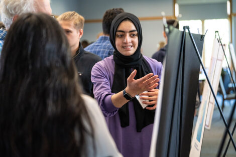 A student smiles and points to their research presentation
