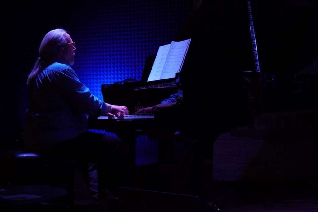 Skip Wilkins sits at a piano in moody blue light