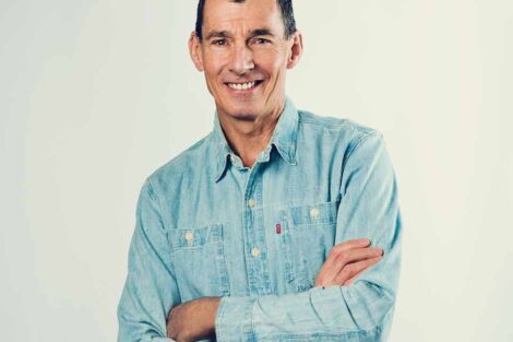 Chip Bergh is standing with his arms crossed and wearing a blue button down shirt.