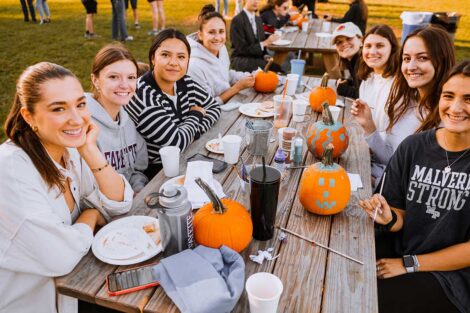 Group of students sitting at a picnic table and painting pumpkins on the Quad at Lafayette's Fall Fest 2022