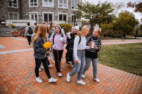 A group of students walk along a brick path, smiling and talking.