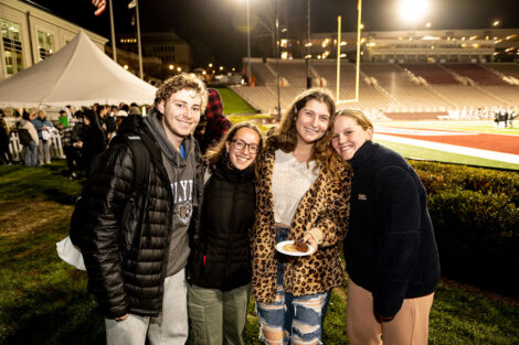 A group of students smile in front of Fisher Field.