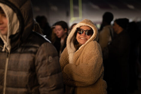 A student smiles, wearing sunglasses and wrapped in a cozy sweater.