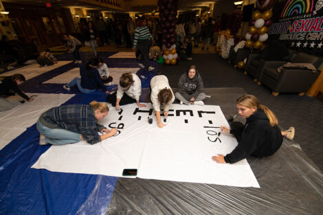 Students paint with black paint on white sheets.