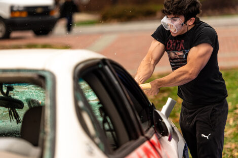 A student, wearing safety goggles, uses a sledgehammer on the Lehigh car.