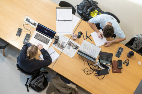 Two students study with material on a table.