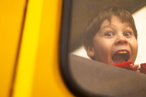 A student smiles inside of a yellow school bus.
