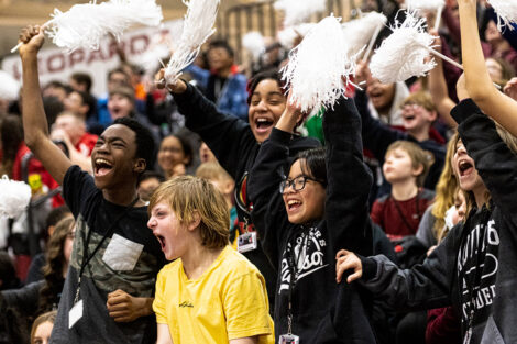 A crowd of children cheer with pom poms.
