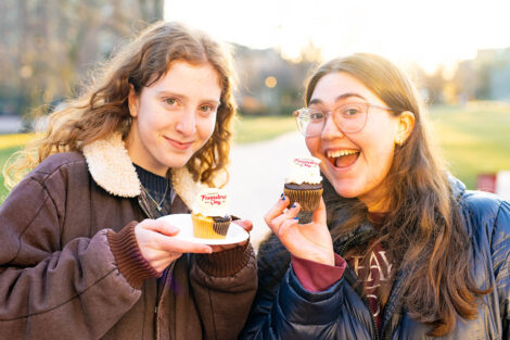 Two students smile, holding cupcakes.