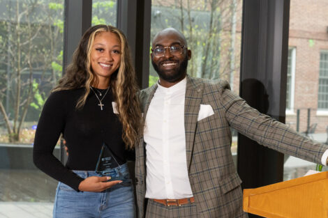 A student smiles, holding an award, alongside Rob Young.