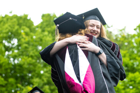 A student hugs President Nicole Hurd on stage, receiving their diploma.