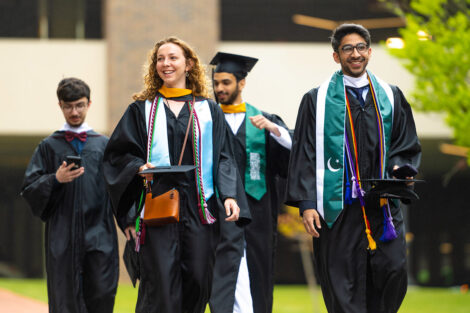 Students walk, wearing their caps and gowns.