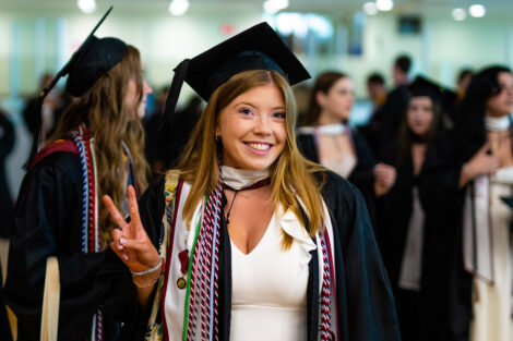 A student smiles, giving the peace sign, wearing their cap and gown.