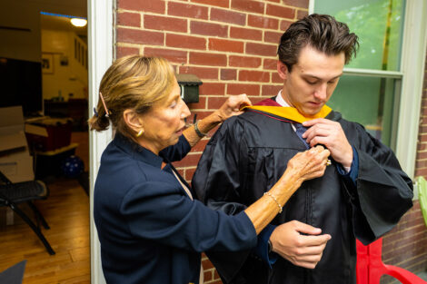 A student's family member helps them get ready in their cap and gown.