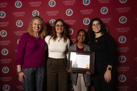 Janine Block smiles with three students, holding an award.